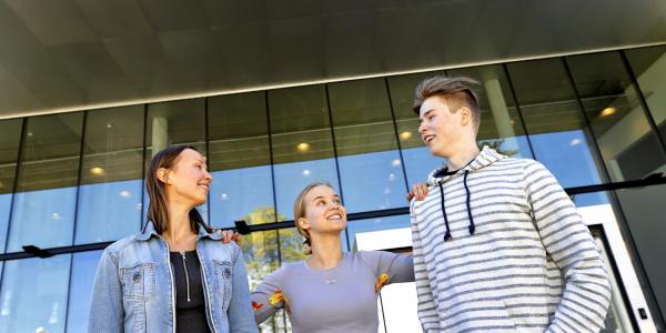 Kolme hymyilevää opiskelijaa seisoo yliopiston kampuksella