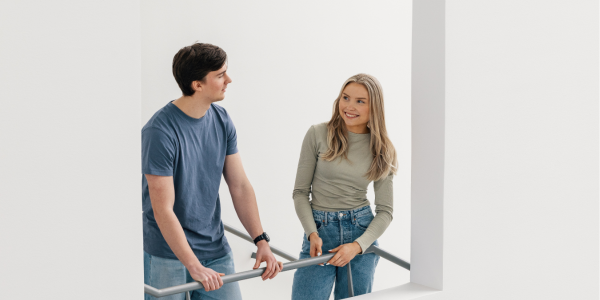 Poika ja tyttö nojaavat porrastasanteella kaiteeseen ja juttelevat keskenään