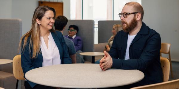 Kuvituskuva, kaksi henkilöä keskustelee pöydän ääressä.