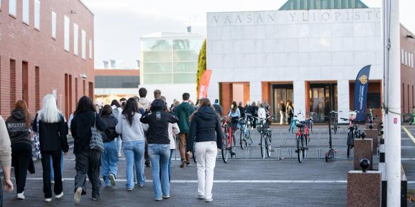 Useita henkiöitä kävelemässä kohti rakennusta. Rakennuksen yläreunassa lukee teksti "Vaasan yliopisto".