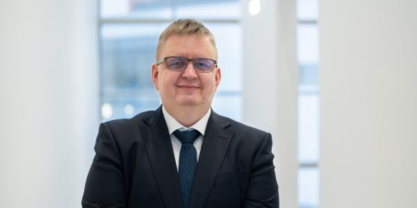 Timo Alho Vaasan yliopistolla, päällä tumma puvuntakki ja kaulassa solmio, katsoo kameraan ja hymyilee tyytyväisenä