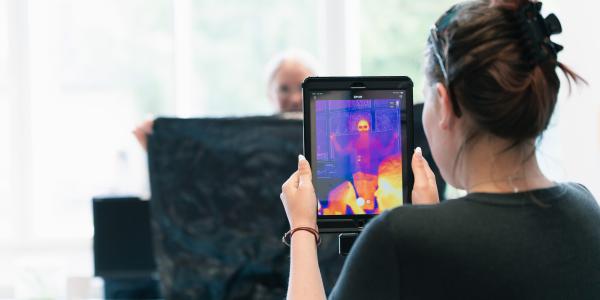 Tyttö kuvaa iPadissa kiinni olevalla lämpökameralla naista, joka seisoo jätesäkin takana.