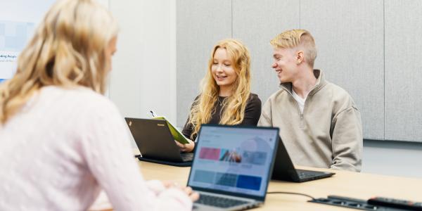 Kolme opiskelijaa pöydän ääressä tekemässä töitä tietokoneella.
