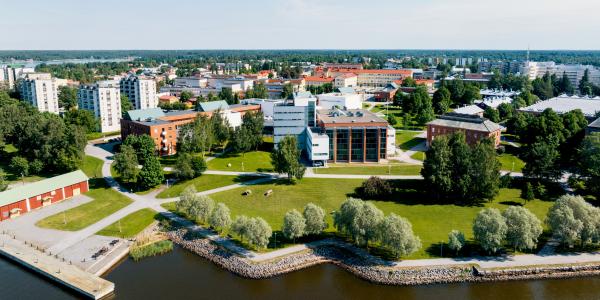 Ilmakuva Vaasan yliopiston kampuksesta. Kuvassa näkyy sininen melkein pilvetön taivas, merta ja yliopiston rakennuksia. Taustalla kaukana näkyy Vaasan kaupunkia.