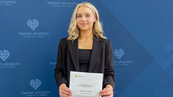 Alisa Flinck Pahkasalo seisomassa yliopiston logoseinän edessä