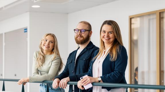 Opiskelijat hymyilevät kaiteseen nojaten ja katsovat kameraan