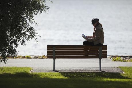Ihminen istuu yksin puistonpenkillä lukemassa